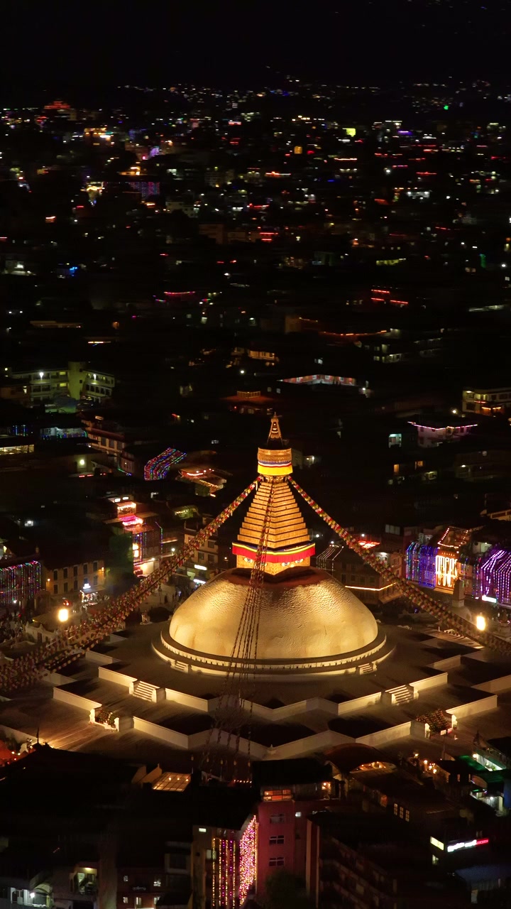 Kathmandu, Nepal, ripresa aerea verticale 9:16 della guglia dorata illuminata della Stupa di Boudhanath, circondata dalle luci scintillanti della città durante la notte del festival delle luci Tihar.