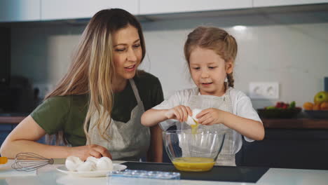 woman looks at little girl cracking chicken egg into bowl