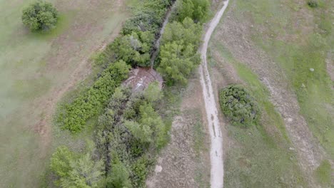 Aerial-view-over-a-small-stream-with-a-small-waterfall-in-the-middle-of-a-large-open-space-field