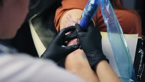 close up female tattoo artist holding tattoo gun working on hand tattoo. gloved hand holding tattoo gun working on modern body art. artist working on female's hand. slow motion