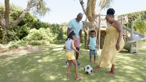 happy african american grandparents with grandchildren playing football in garden, in slow motion