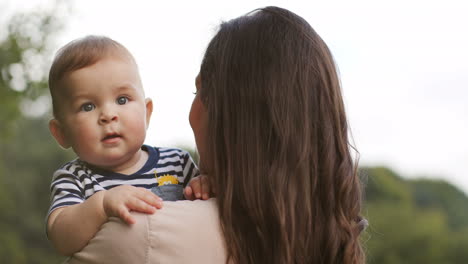 back view of a woman with long dark hair holding her smiling little son outdoors