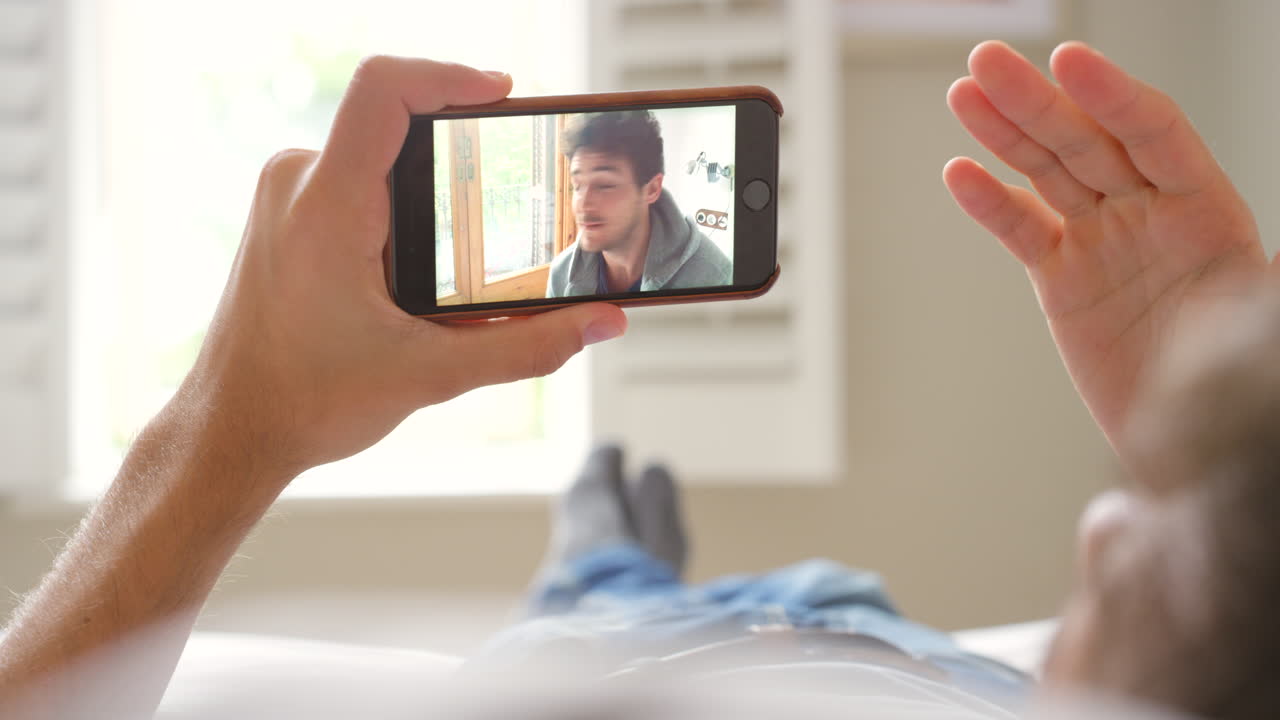 hombre viendo una llamada de video en su teléfono inteligente mientras se relaja en el sofá