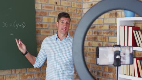 Caucasian-male-maths-teacher-standing-at-blackboard-giving-an-online-lesson-to-camera