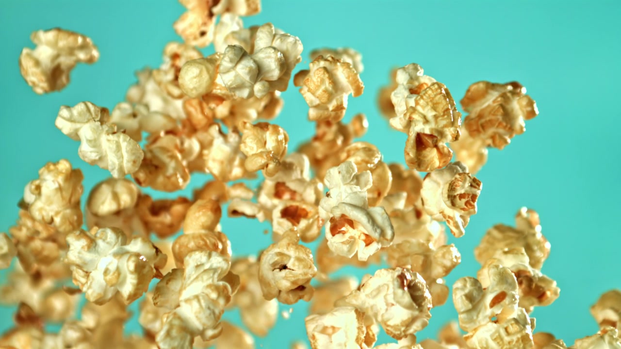 Popcorn deliziosi che volano in alto su sfondo verde acqua al rallentatore