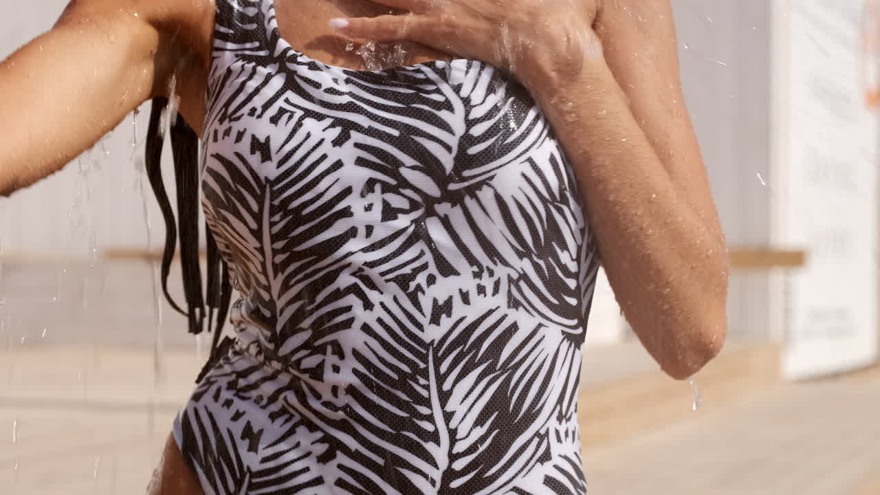 수영복을 입은 갈색 소녀가 해변에 호스에서 물을 고 있습니다.