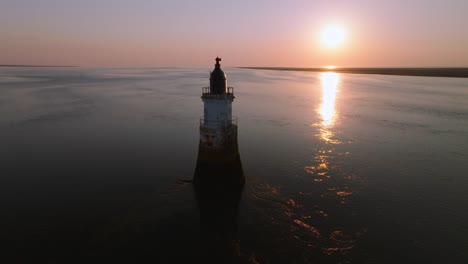 old abandoned lighthouse in calm tidal waters at sunset with seabirds flying past. plover scar lighthouse, lancashire, uk.