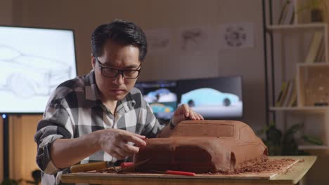 asian man automotive designer works on the sculpture of car clay using his hands to smooth out the surface and create details in the design in the studio