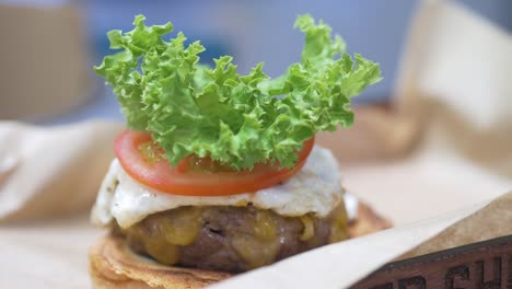 primer plano de una hamburguesa de queso gourmet con tomate y el chef agrega lechuga y el pan superior
