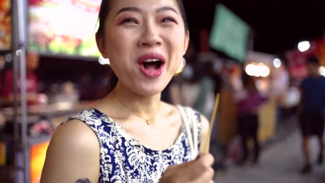 cheerful asian woman eating potato balls on street