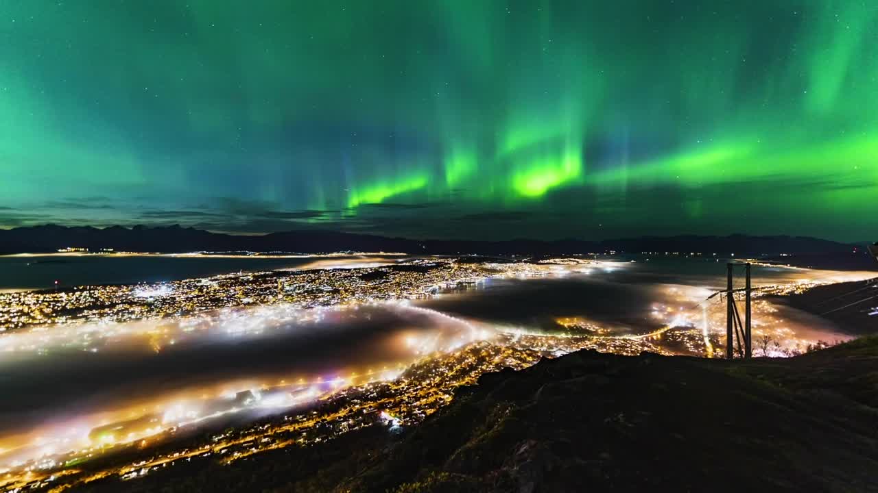 el lapso de tiempo de la aurora, las luces del norte con la ciudad de tromsø, noruega en el frente