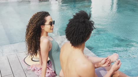 video of happy diverse couple relaxing in the sun and talking at the poolside of holiday home