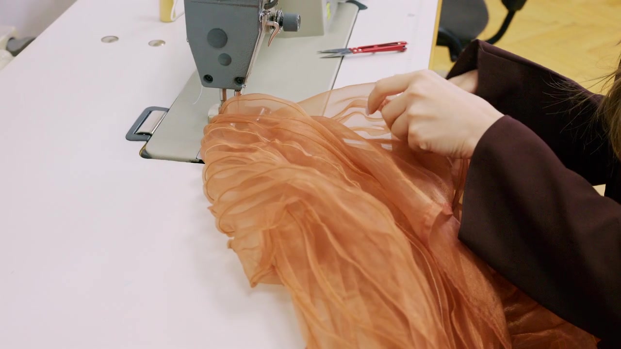 Uno stilista guida un tessuto di organza arancione traslucido sotto l'ago di una macchina da cucire industriale