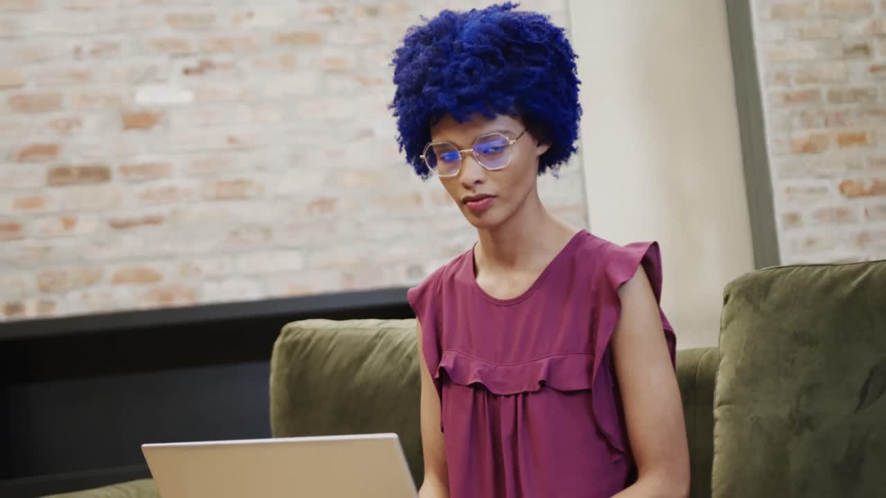 Ritratto di felice imprenditrice birazziale con afro blu che usa il laptop, al rallentatore