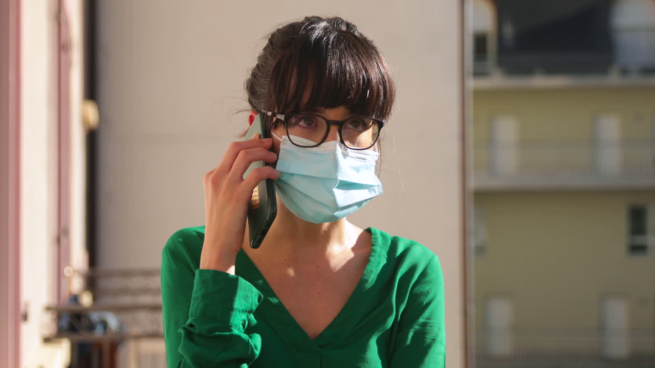 Close up of a brunette woman, wearing glasses, makes a phone call with a mask during lockdown