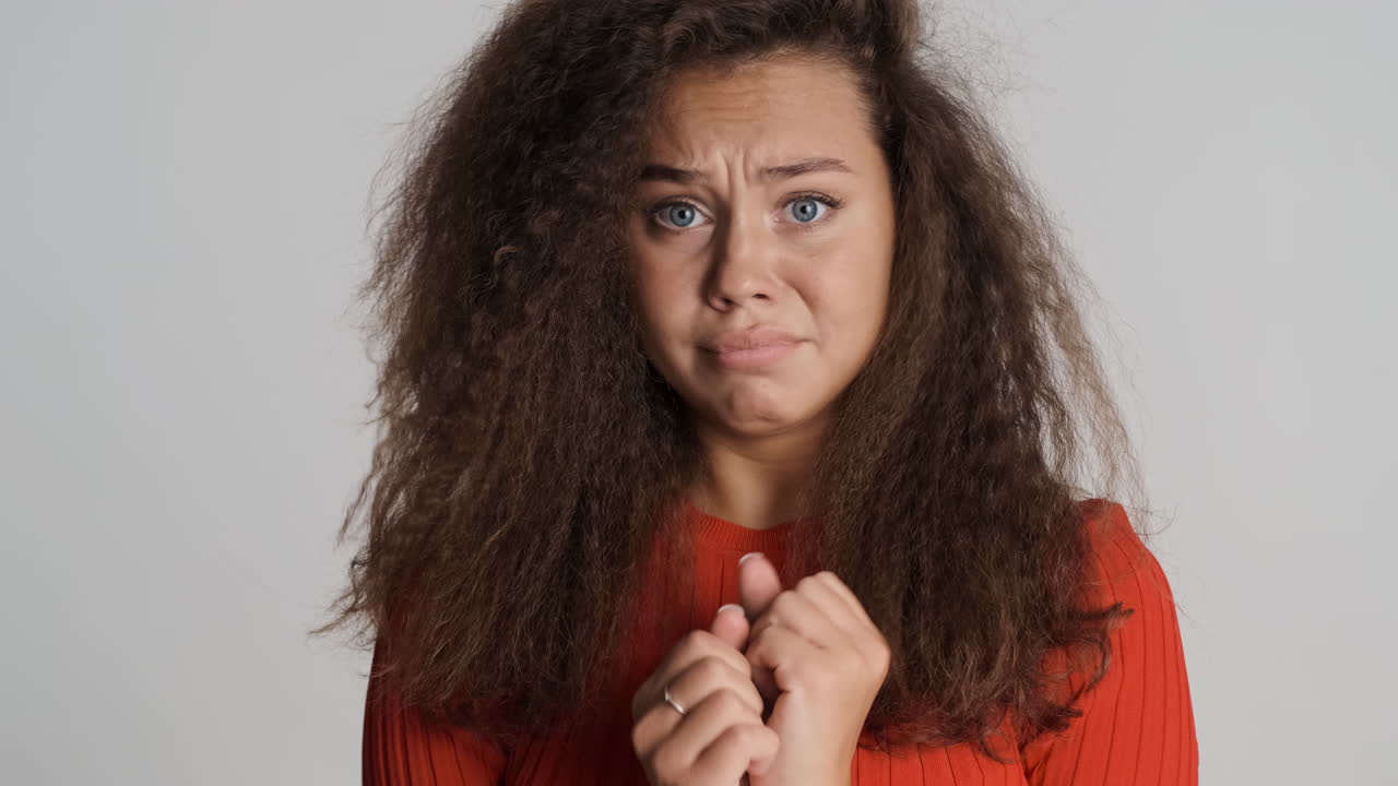 Caucasian curly haired woman looking scared at the camera.