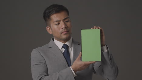 studio shot of serious businessman in suit holding green screen digital tablet