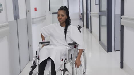 african american female patient in wheelchair in hospital corridor, slow motion