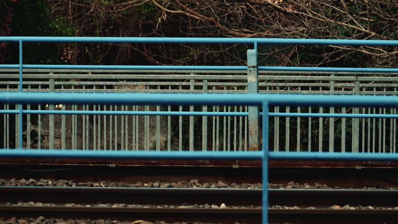 Side view of a passenger train moving past a blue fence near the railway tracks