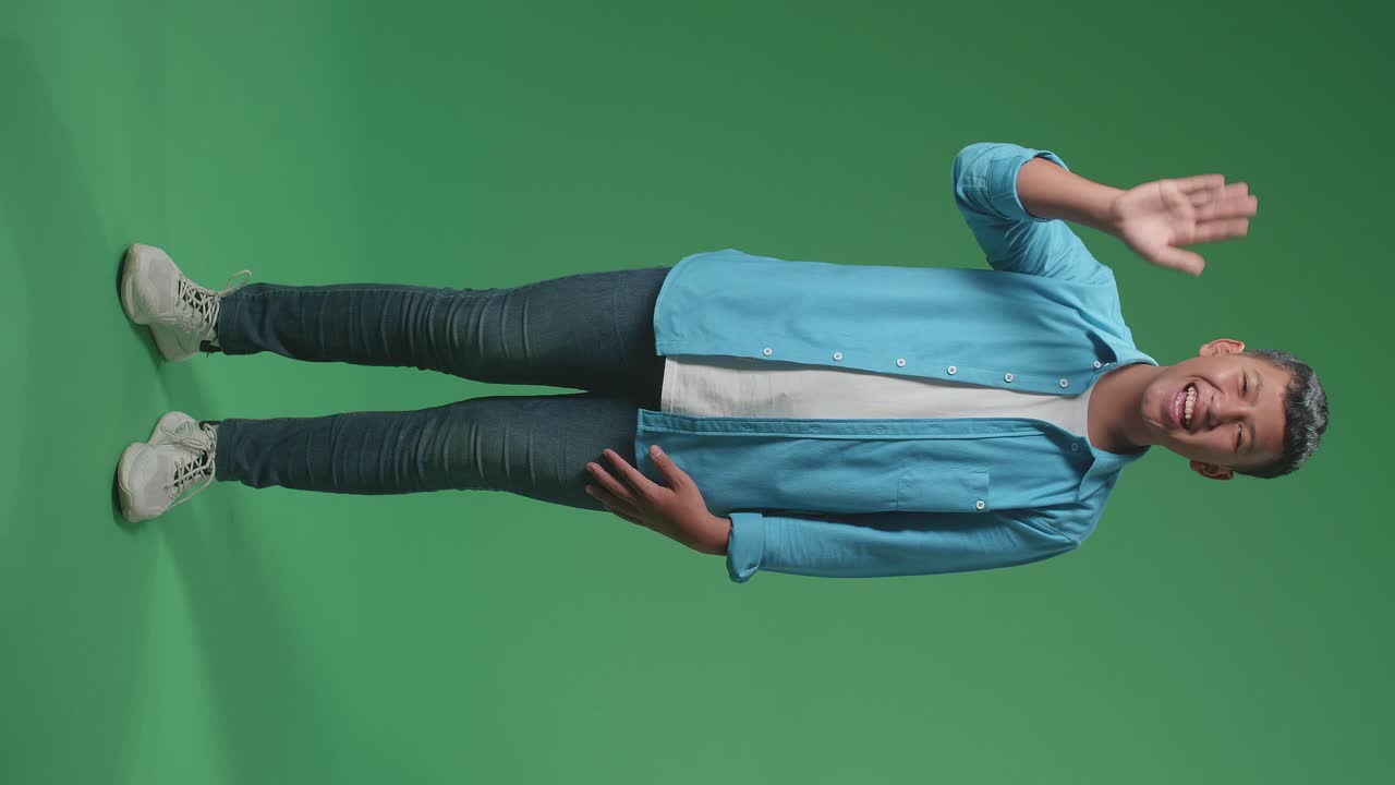 The happy young Asian man waving hand while standing on green screen in the studio