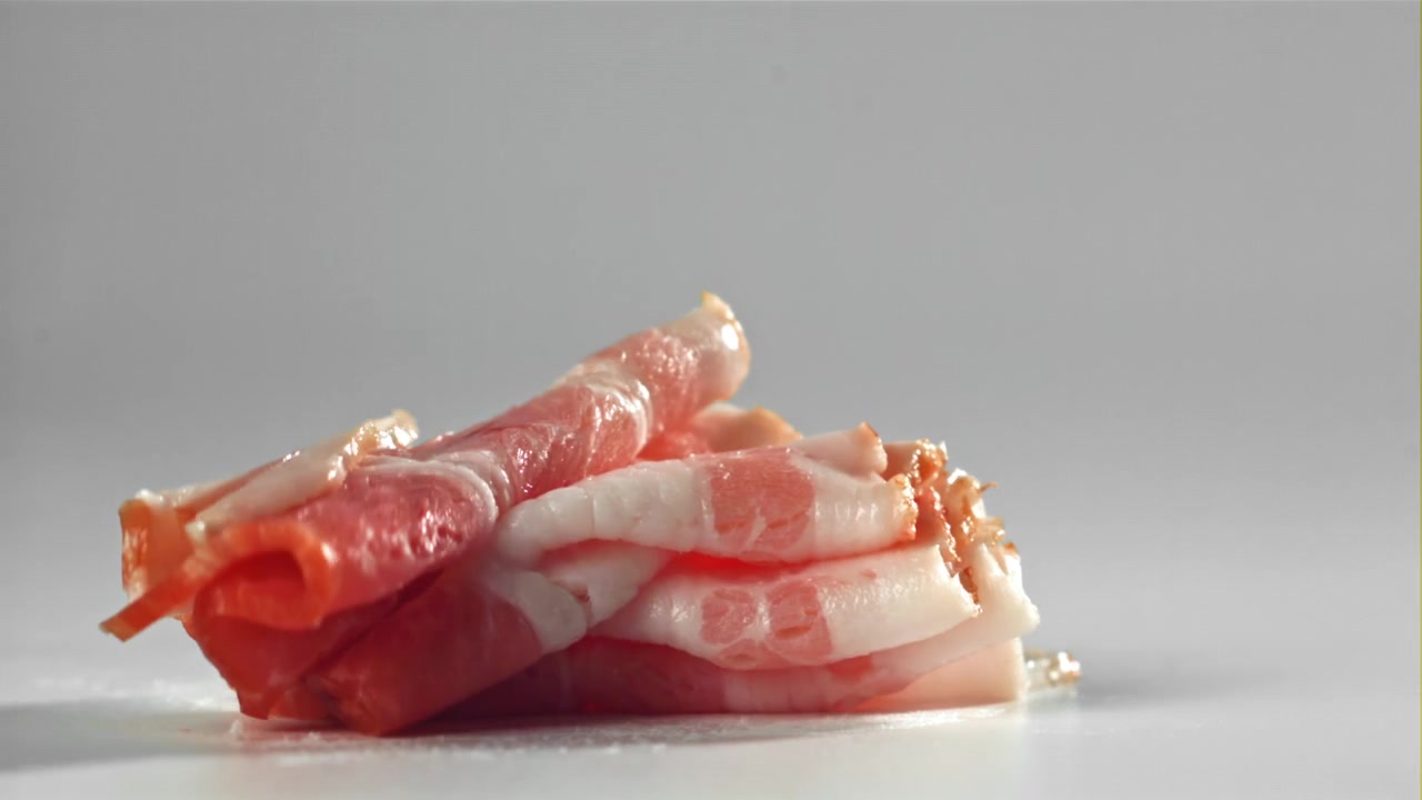 Primo piano di una fetta di pancetta cruda che cade al rallentatore