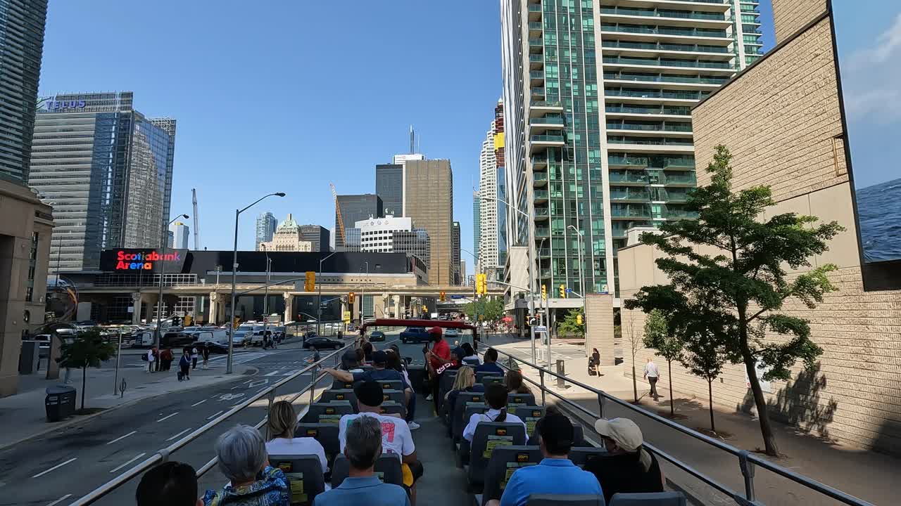 Bustling open-top sightseeing bus tour through modern Toronto, with tourists enjoying panoramic views of towering skyscrapers, iconic city landmarks, vibrant city streets under blue sky, Canada