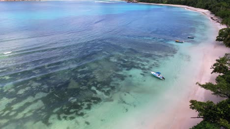low moving drone footage of white sandy beach, large granite stone, trees and docked fisherman boats near the shore, baie lazare