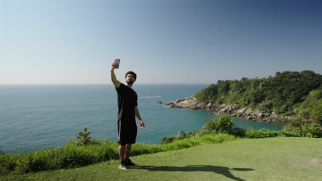 young traveler stands on lush coastal cliff takes selfie with sparkling ocean backdrop
