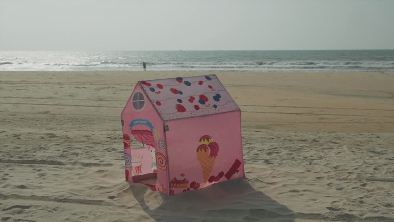 Handheld shot of pink kids' house tent blowing in the wind at beautiful Benaulim Beach in Goa on a sunny summer day