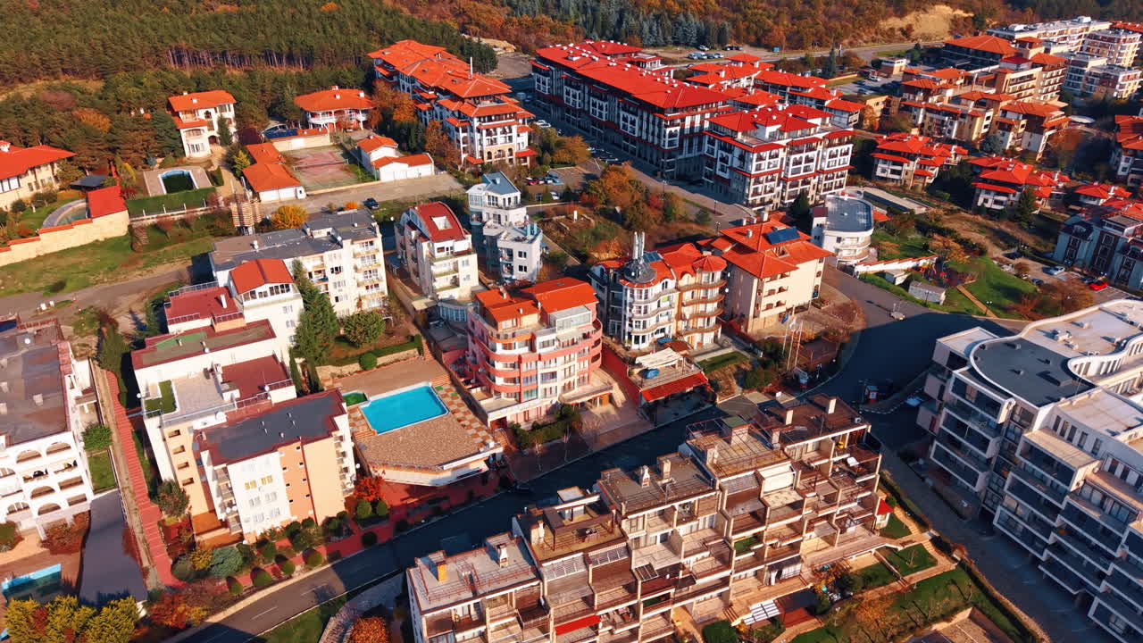 Orman yakınındaki yerleşim apartman bloklarının havadan görünümü. Yeşil bir orman ve yüzme havuzu alanı arasında yer alan kırmızı çatılı modern çok katlı yerleşim binaları.