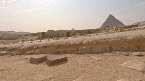 Pirámides-Icónicas-En-La-Distancia-Detrás-De-Ruinas-De-Muros-Y-Estructuras-De-Casas-En-Egipto