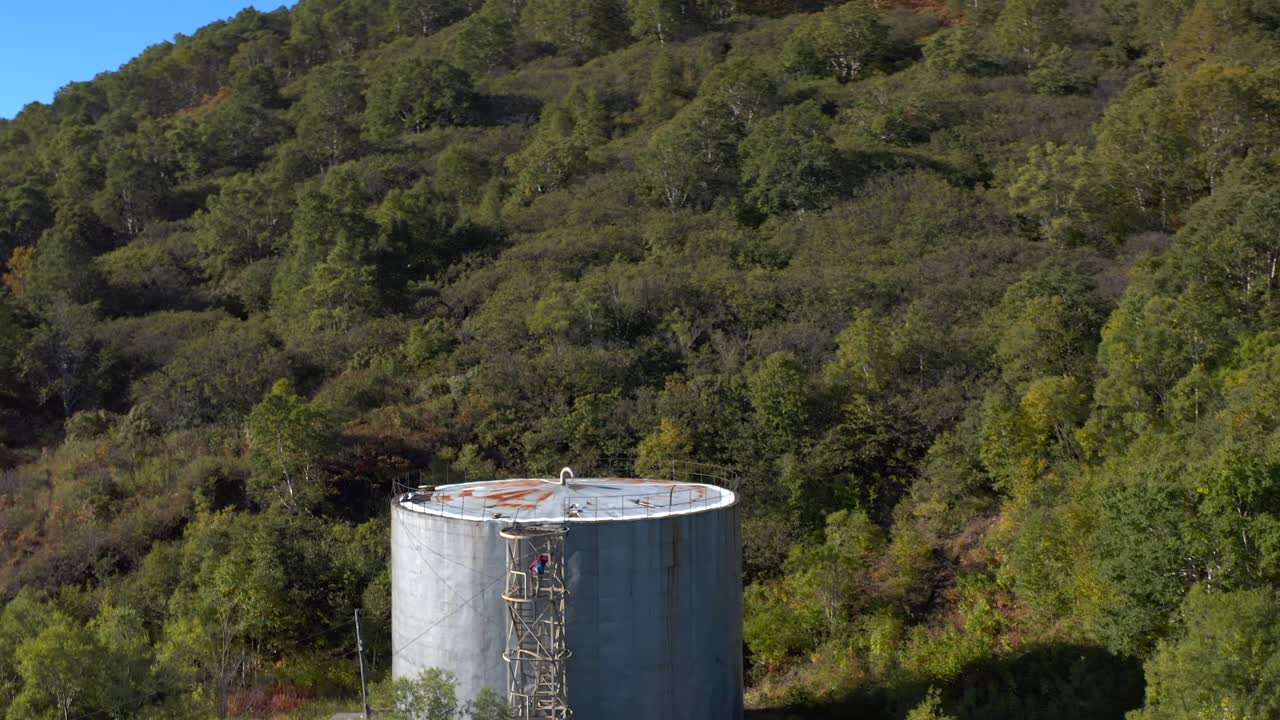 남자가 높은 은 둥근 배럴에 철 사다리를 올라간다. 목표 언덕.