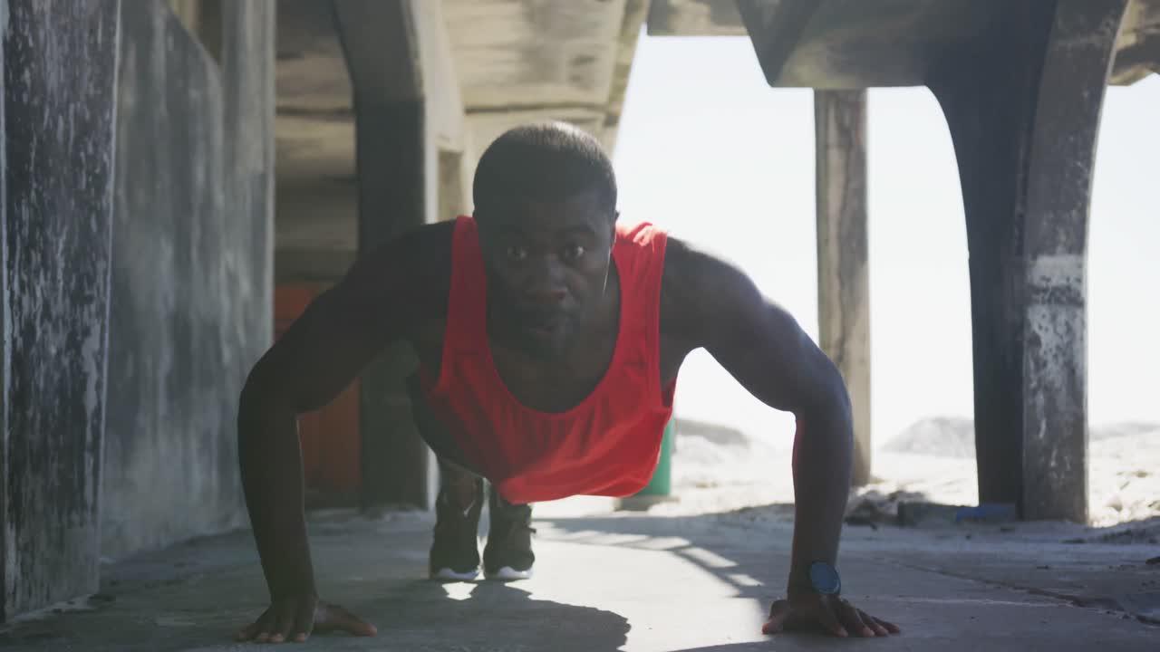 Focused african american man doing press ups, exercising outdoors by the sea