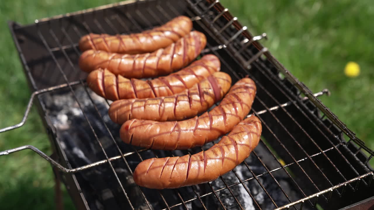 Roast wiener on a barbecue grill on charcoal. Cook turns over hot grilled sausages with a food tong in the garden in summer. Delicious food for a picnic.