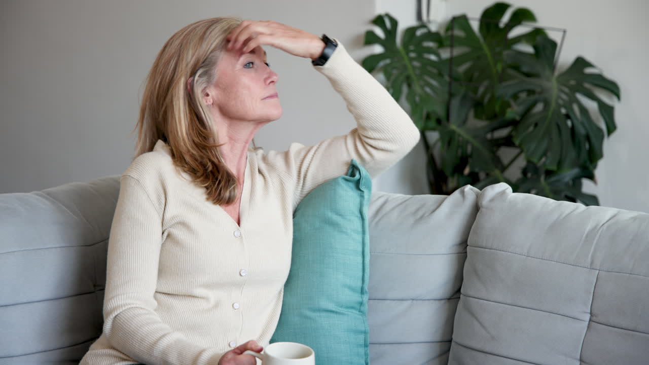 Smiling senior woman enjoying coffee on cozy sofa at home