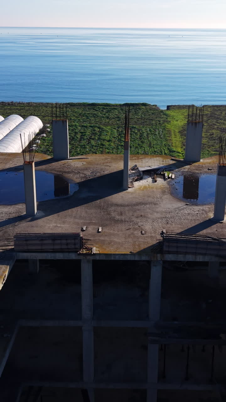 Tetto in cemento con pilastri e acqua stagnante che si affaccia sul mare. Vista aerea del tetto di un edificio incompiuto. Video verticale