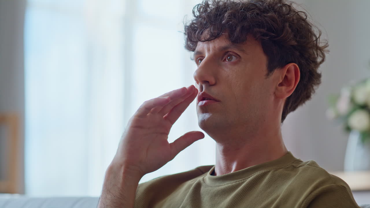 Pensive man sitting home in modern living room closeup. Worried guy thinking