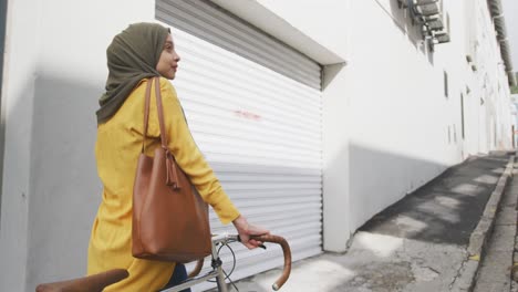 woman wearing hijab walking and holding a bike behind her