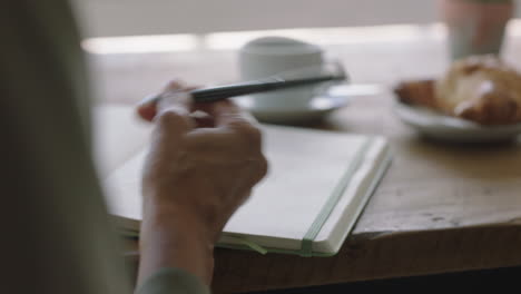 young woman hands writing to do list making notes in diary planning using journal reminder in coffee shop close up