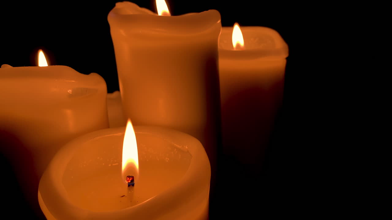 Gruppo di candele accese con fiamma arancione, quattro candele su sfondo nero al rallentatore