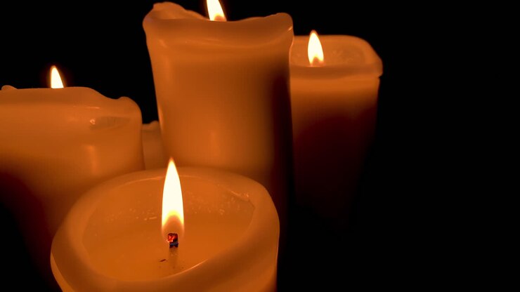 Gruppo di candele accese con fiamma arancione, quattro candele su sfondo nero al rallentatore