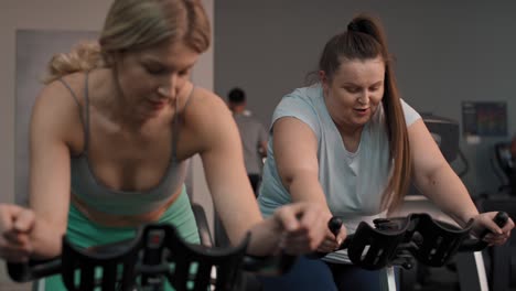 dos mujeres caucásicas montan en bicicleta en el gimnasio.