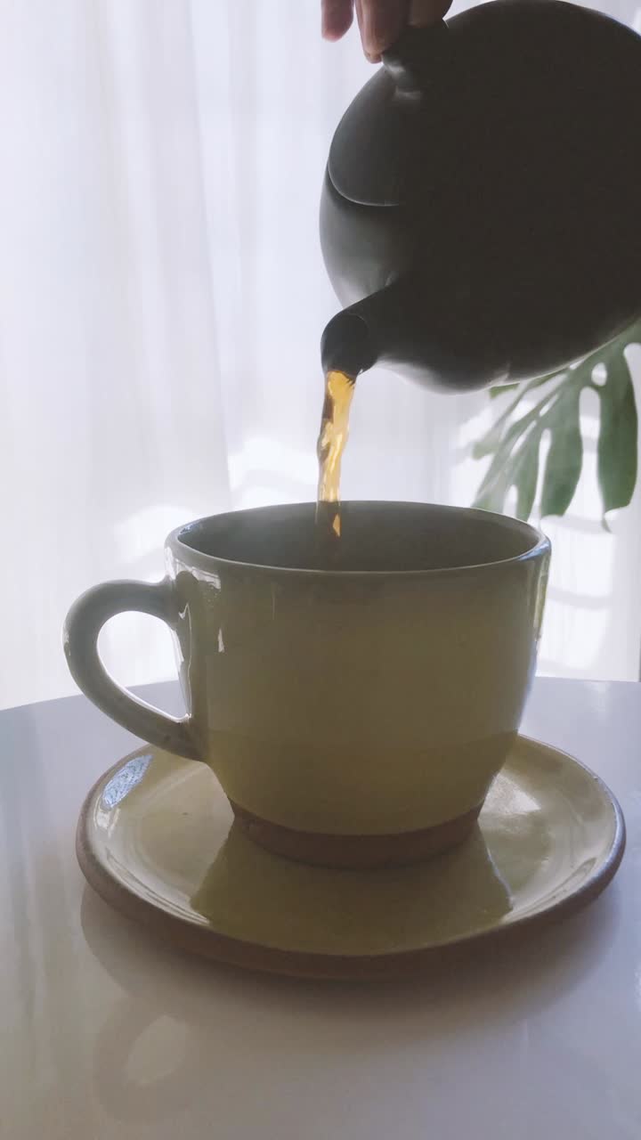 Mano che versa una bevanda calda in una tazza di ceramica gialla
