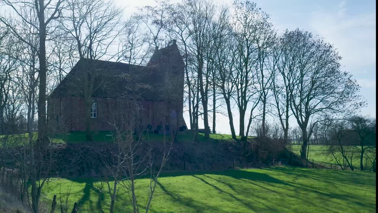 Gammel murstenskirke på en bakke med nøgne træer og grønne marker