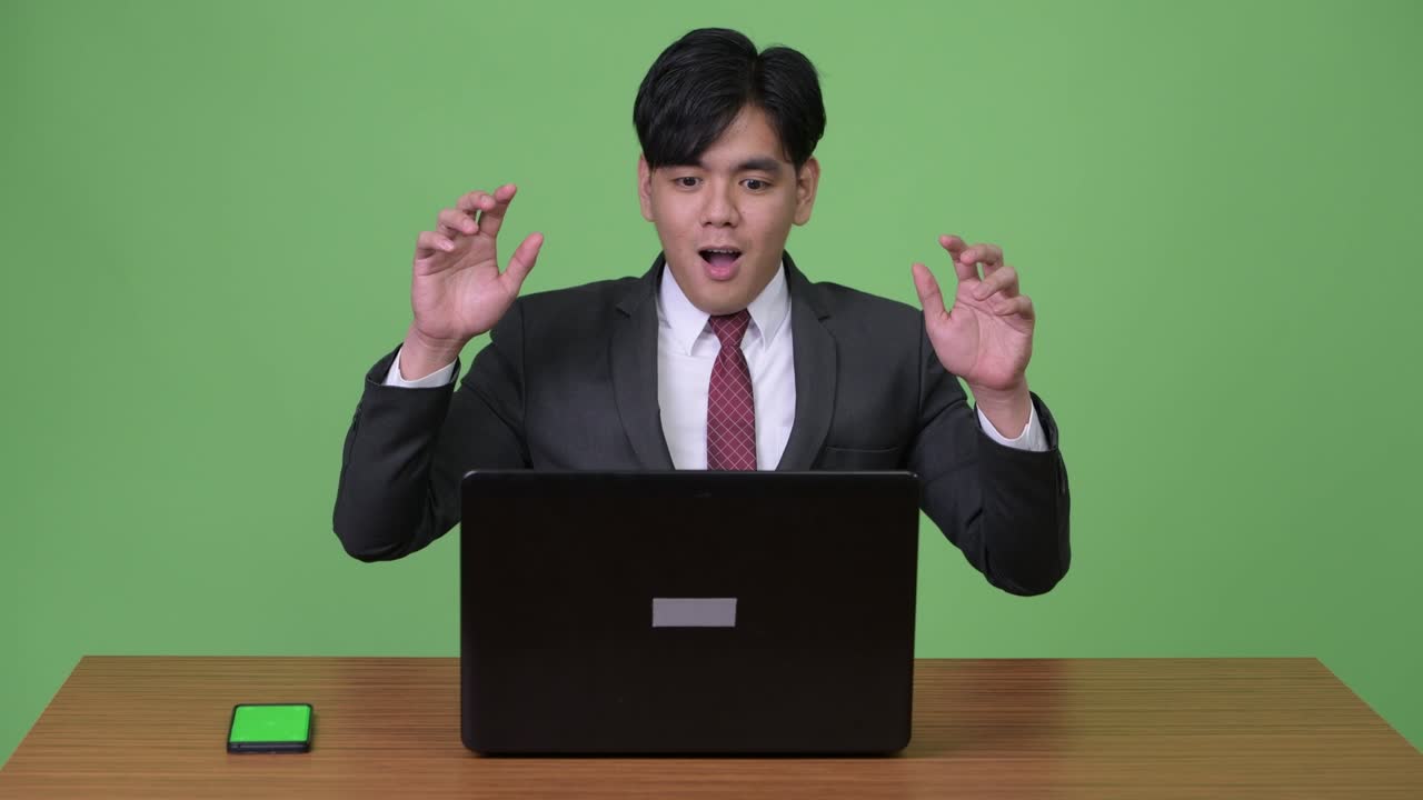 젊은 잘생긴 아시아 사업가가 초록색 배경에 노트북을 가지고 일하고 있습니다.