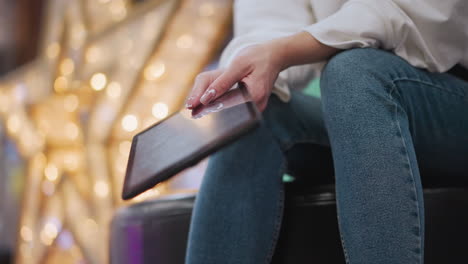 close-up of a hand holding a tablet gently tilted with light reflections on the screen, decorative lights glow softly in the blurred background