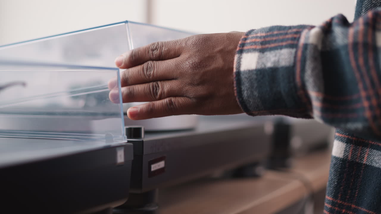 Man opens lid of vintage turntable closeup. African American melomaniac prepares retro music playing device for work at home. Audio appliance