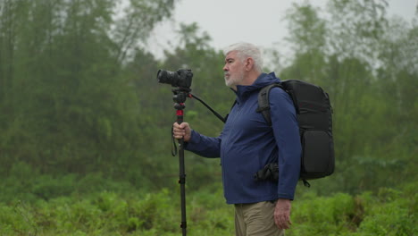 aged man walking while holding a camera with monopod stand in nature background