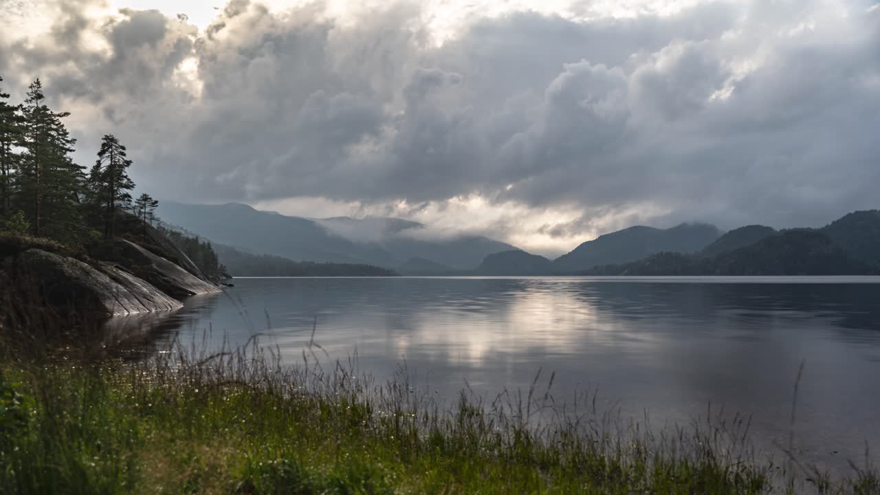 nubes oscuras y tormentosas giran sobre el lago con orillas rocosas y montañas.