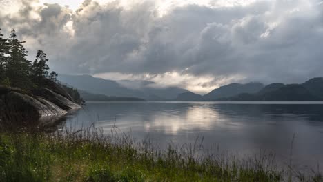 dark stormy clouds whirl over the lake with rocky banks and mountains